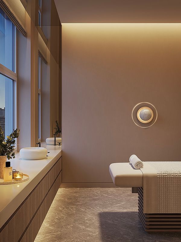 This serene, spa-inspired bathroom features a minimalist aesthetic with a sleek floating vanity, a circular vessel sink, and a massage table, suggesting a high-end wellness retreat. The space is bathed in warm, ambient cove lighting and features a modern circular wall sconce, creating a tranquil and luxurious atmosphere. The perspective is a wide, eye-level shot that emphasizes the clean lines, marble-textured flooring, and the seamless integration of relaxation and utility.