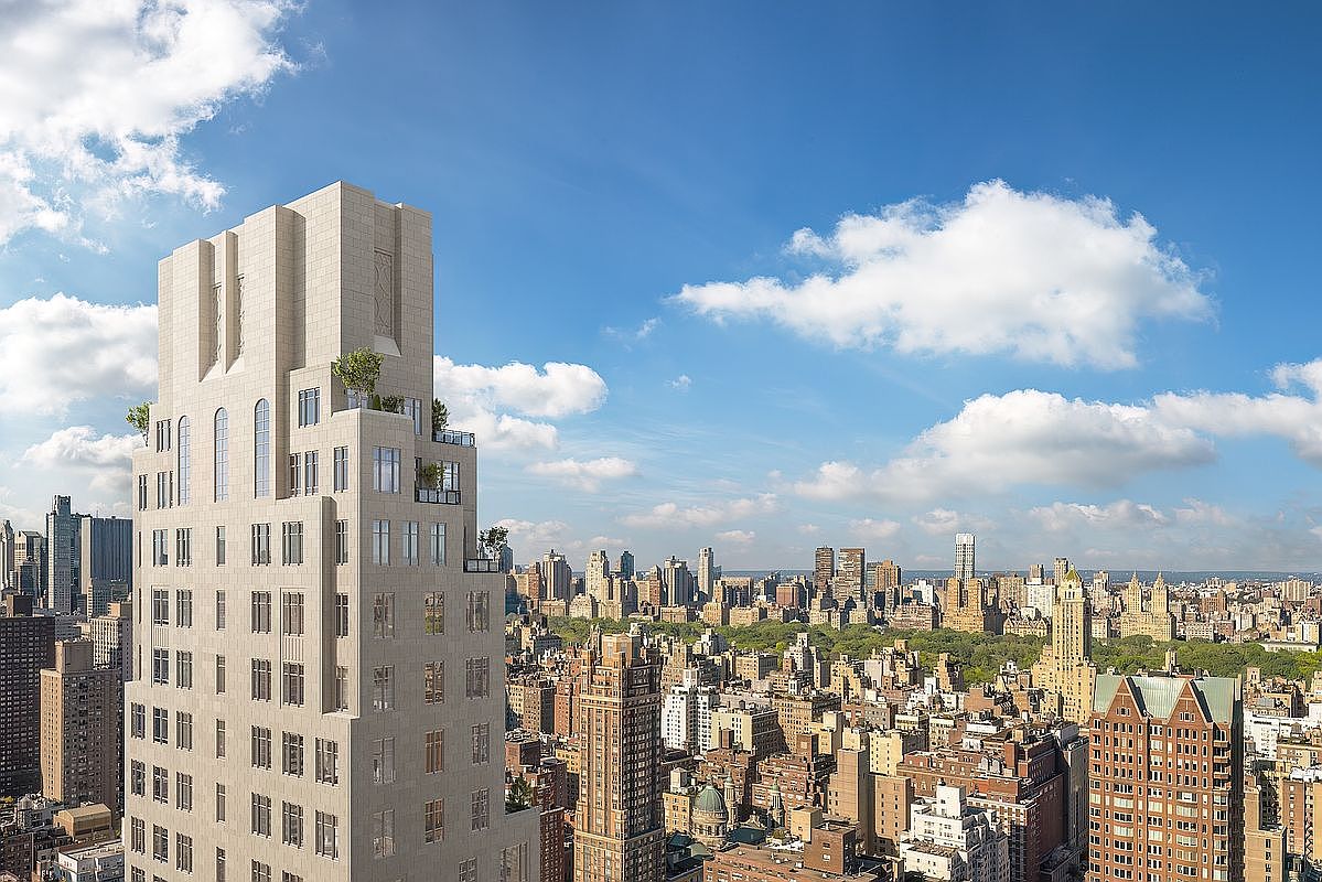 This high-angle aerial shot captures a sophisticated, light-colored stone skyscraper rising prominently above the dense urban landscape of New York City. The building features a tiered, stepped-back architectural design with integrated terraces and greenery, set against a vibrant blue sky with scattered clouds. The perspective provides a sweeping panoramic view of the surrounding city skyline, emphasizing the building's luxury status and prime location.