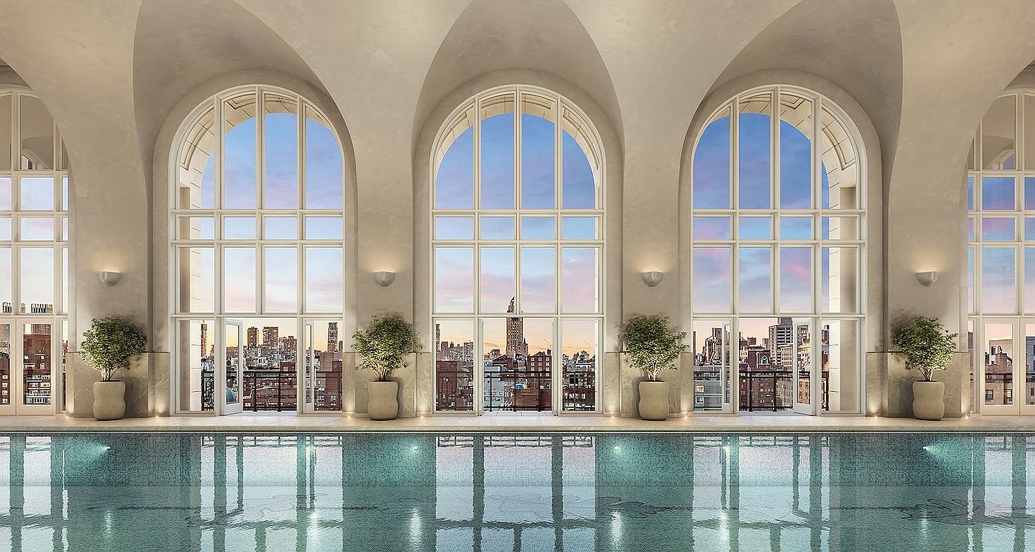This luxurious indoor swimming pool area features a series of grand, arched floor-to-ceiling windows that frame a stunning urban skyline at dusk. The space is characterized by its elegant, vaulted ceiling, neutral stone-toned walls, and symmetrical arrangement of potted greenery, creating a serene and sophisticated atmosphere. The perspective is a perfectly centered, wide-angle shot that emphasizes the architectural symmetry and the seamless transition between the indoor pool and the city view.