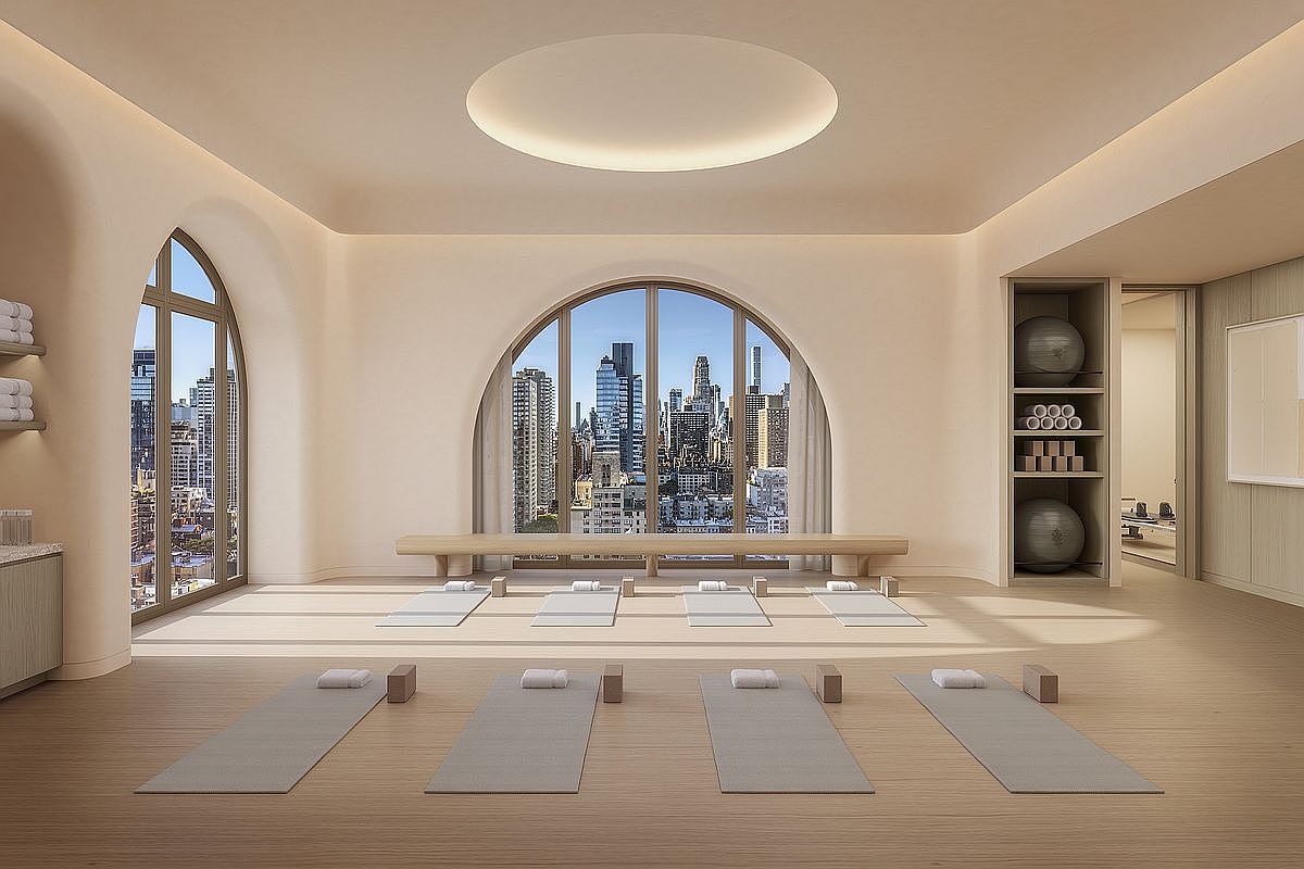 This serene, minimalist yoga and fitness studio features light wood flooring, soft neutral walls, and a striking arched window framing a panoramic city skyline. The space is thoughtfully arranged with yoga mats, blocks, and a built-in storage unit containing exercise balls and equipment, creating a tranquil atmosphere for wellness. The perspective is centered and symmetrical, emphasizing the calm, high-end aesthetic of this luxury amenity space.