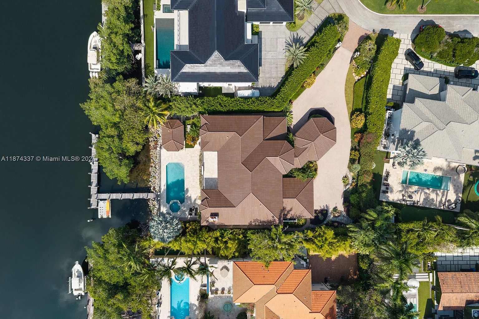 This aerial shot showcases a luxurious waterfront property with a sprawling brown-tiled roof, a private pool and spa, and a dock extending into the water. Lush landscaping surrounds the house, providing privacy and enhancing the overall curb appeal. The perspective gives a comprehensive view of the property's layout and its prime location.