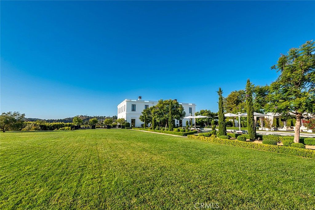 This image showcases a sprawling, meticulously maintained yard and garden. A large, well-manicured lawn leads up to a grand white building, complemented by neatly trimmed hedges, topiaries, and mature trees. The scene exudes a sense of luxury and tranquility, highlighting the expansive outdoor space as a key feature of the property.