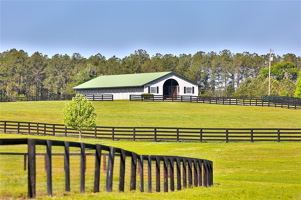 This image showcases a well-maintained yard with a large barn-style building in the background. The property is surrounded by a black wooden fence, adding a touch of rustic charm. The expansive green lawn and mature trees create a serene and inviting atmosphere, perfect for a country estate.