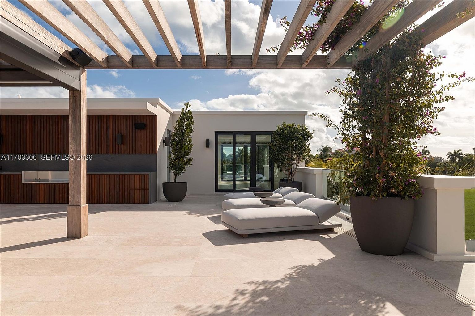 This luxurious rooftop terrace features a modern pergola structure, sleek lounge seating, and integrated planters with lush greenery. The space is designed for high-end outdoor living, showcasing a minimalist aesthetic with clean lines and a neutral color palette. The perspective captures the inviting atmosphere of the deck, highlighting the seamless blend of indoor-outdoor transition.