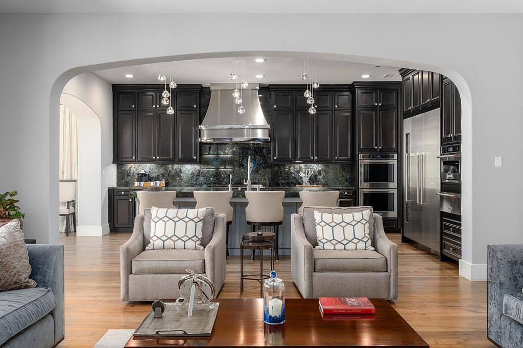 This interior shot showcases a living room that seamlessly transitions into a modern kitchen. The living area features comfortable armchairs and a coffee table, while the kitchen boasts dark cabinetry, stainless steel appliances, and a stylish backsplash. The open-concept design creates a spacious and inviting atmosphere, perfect for entertaining.