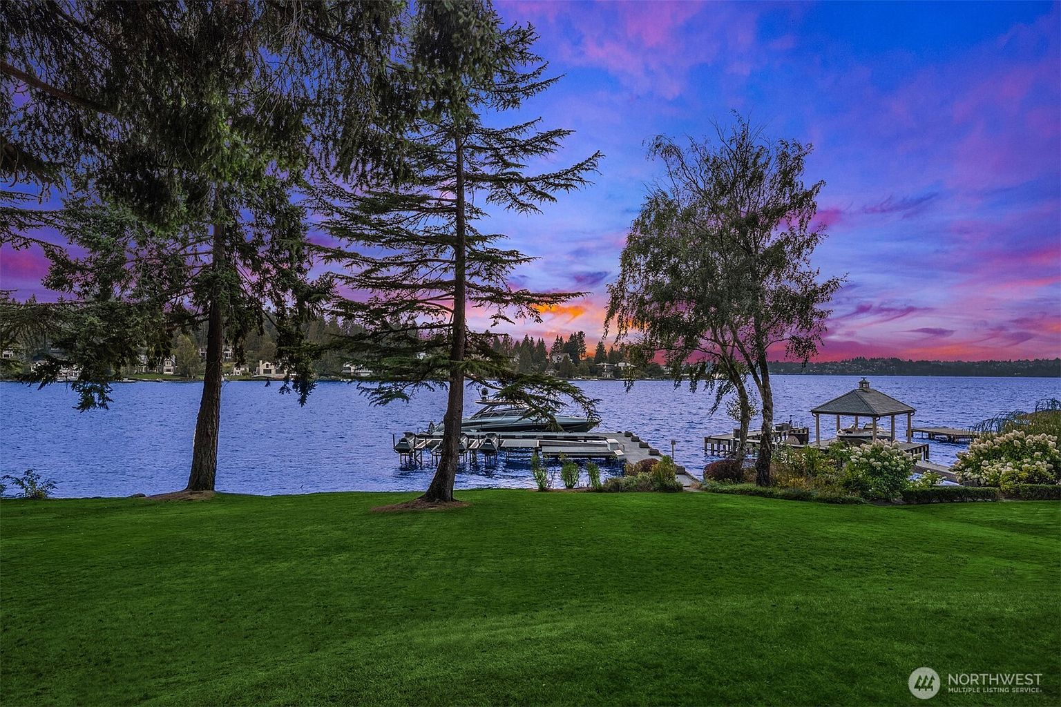 This stunning rear view showcases a waterfront property with a lush green lawn leading to a serene lake. A private dock with a boat and a charming gazebo enhance the property's appeal. The vibrant sunset sky adds a touch of drama and luxury, making it an ideal setting for relaxation and entertainment.