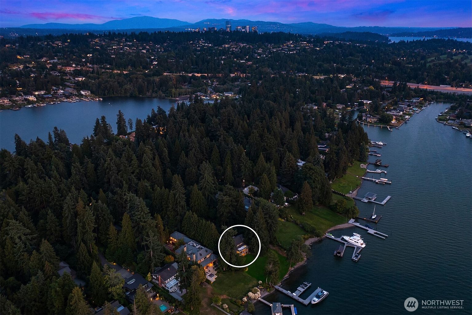 This aerial shot showcases a beautiful property nestled among lush trees on a waterfront. The house, circled for emphasis, is surrounded by dense greenery, offering privacy and a sense of seclusion. Several docks and boats are visible along the shoreline, highlighting the property's access to the water and recreational opportunities.