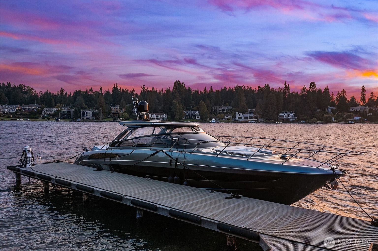 This image showcases a sleek, modern yacht docked at a pier against a vibrant sunset backdrop. The yacht features a dark hull with elegant lines and reflective windows, suggesting luxury and sophistication. The pier is constructed of gray metal and wood, and the overall scene evokes a sense of tranquility and high-end living.