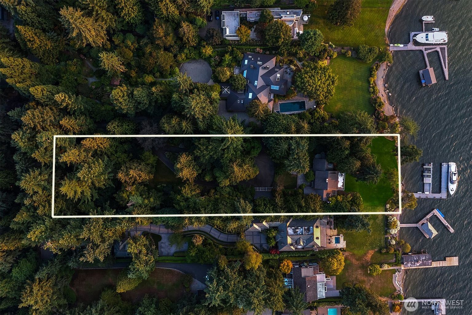 This aerial shot showcases a luxurious property nestled among lush greenery, offering a sense of privacy and seclusion. The estate features well-manicured lawns, mature trees, and a waterfront location with private docks. The overall impression is one of exclusivity and high-end living.