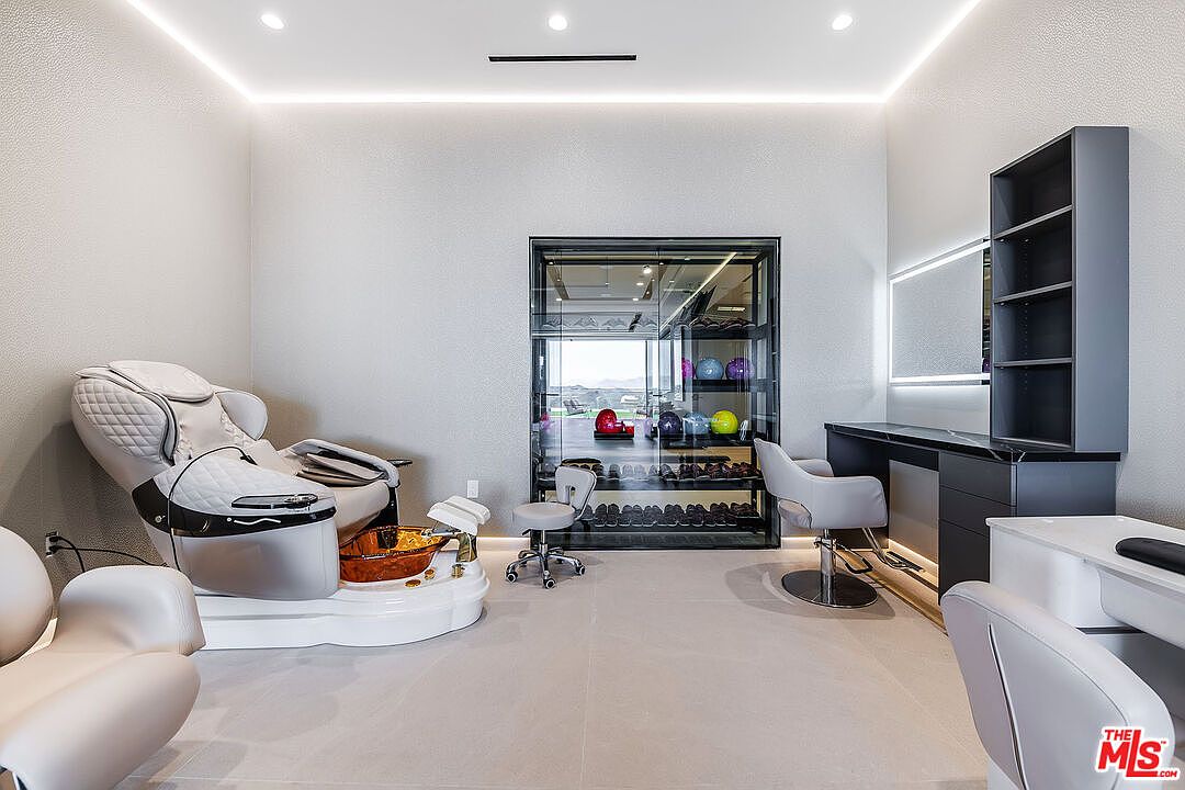 This interior shot showcases a luxurious salon or spa room, featuring a plush pedicure chair with a built-in foot bath, a manicure station with comfortable seating, and a sleek display cabinet filled with bowling balls and shoes. The room is well-lit with modern recessed lighting and a linear light fixture above the vanity, creating a clean and upscale ambiance.