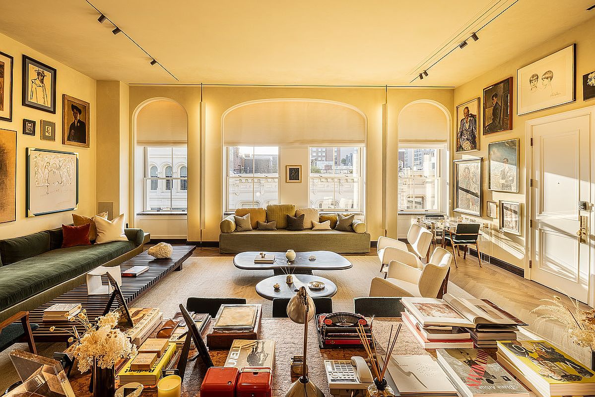 This is a spacious and well-lit living room featuring a blend of classic and contemporary design elements. The room is adorned with numerous framed artworks, adding a touch of sophistication. Large arched windows provide ample natural light, complemented by track lighting, while the furniture arrangement creates a comfortable and inviting atmosphere.