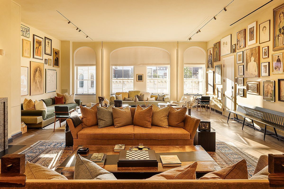 This is a spacious and elegantly decorated living room featuring a blend of classic and contemporary styles. The room is filled with natural light from large arched windows and is adorned with numerous framed artworks on the walls. Multiple seating areas are arranged around a central coffee table, creating a comfortable and inviting atmosphere.