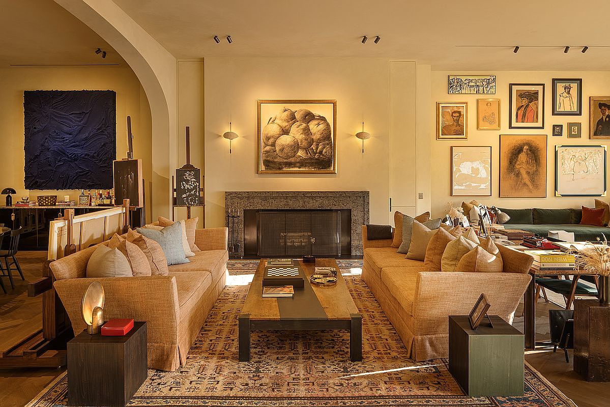 This is an interior shot of a living room featuring two sofas facing each other, separated by a coffee table. The room is decorated with various artworks on the walls and has a fireplace as a focal point. The overall style is eclectic and artistic, creating a warm and inviting atmosphere.