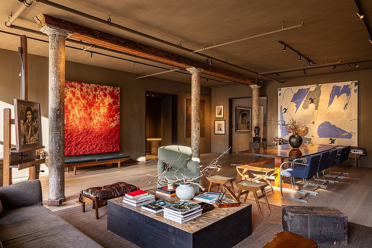 This interior shot showcases a spacious living room with an artistic and sophisticated ambiance. The room features exposed wooden beams supported by pillars, large abstract paintings, and a mix of modern and rustic furniture. The overall impression is one of a stylish and comfortable living space with unique architectural details.