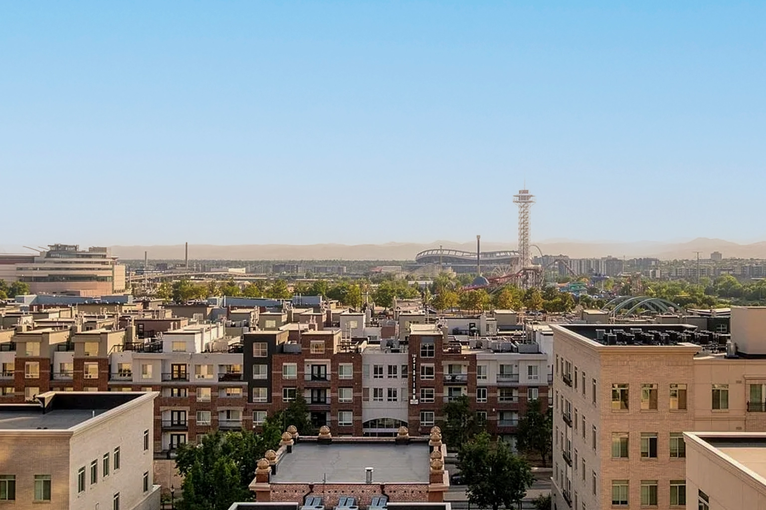 This aerial view showcases a dense urban landscape featuring multi-story residential buildings with varying architectural styles. In the background, a stadium, a tall tower, and a roller coaster are visible, adding to the dynamic skyline. The image offers a sense of the property's location within a vibrant community with access to entertainment venues.