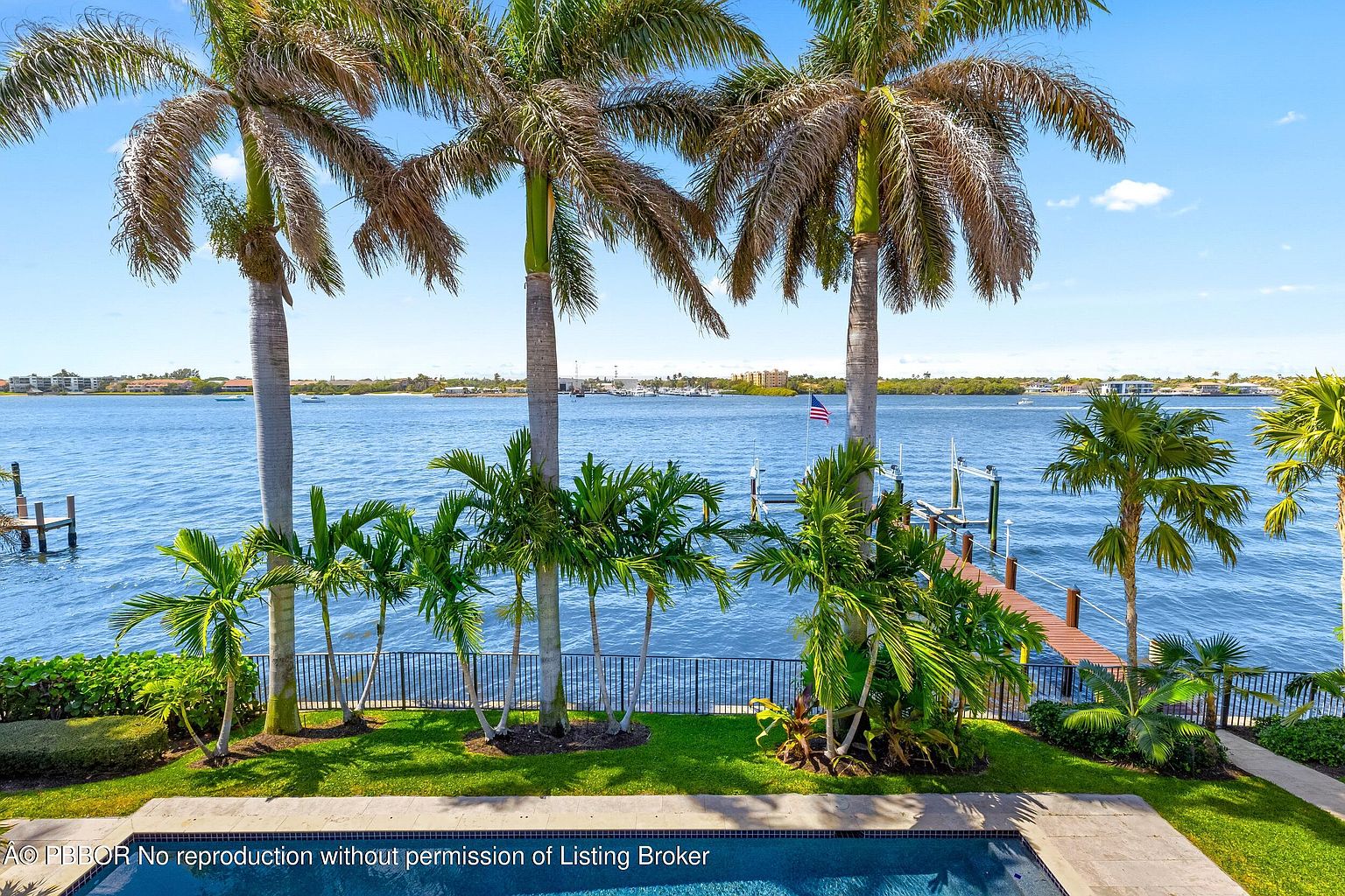 This image showcases a luxurious backyard with a pool and stunning waterfront views. Palm trees line the property, adding a tropical feel, while a private dock extends into the water. The well-maintained lawn and landscaping enhance the overall appeal, creating a serene and inviting outdoor space.