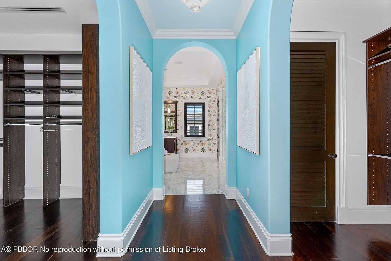 This interior shot showcases a hallway with a striking blue color scheme, complemented by dark hardwood flooring. The hallway features an arched doorway leading to a bathroom with floral wallpaper, and artwork adorns the walls. The image provides a glimpse into the home's unique design and attention to detail.