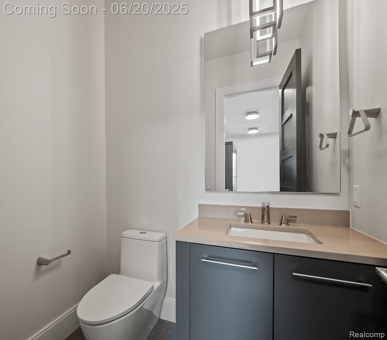 This is a well-lit guest bathroom featuring a modern vanity with a light countertop and dark gray cabinetry. A large mirror reflects the room, and a white toilet is positioned to the left. The overall design is clean and contemporary, creating a welcoming and functional space.
