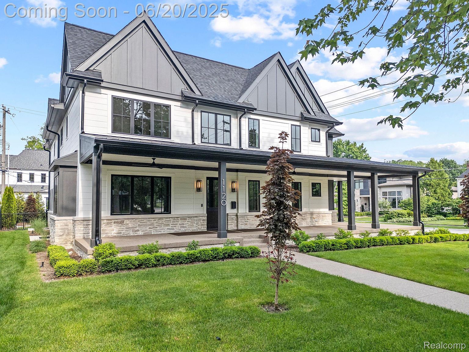 This is a front exterior view of a modern two-story house with a striking black and white color scheme. The house features a large covered porch with black support columns and a stone base. The well-manicured lawn and landscaping enhance the curb appeal, creating an inviting and sophisticated impression.