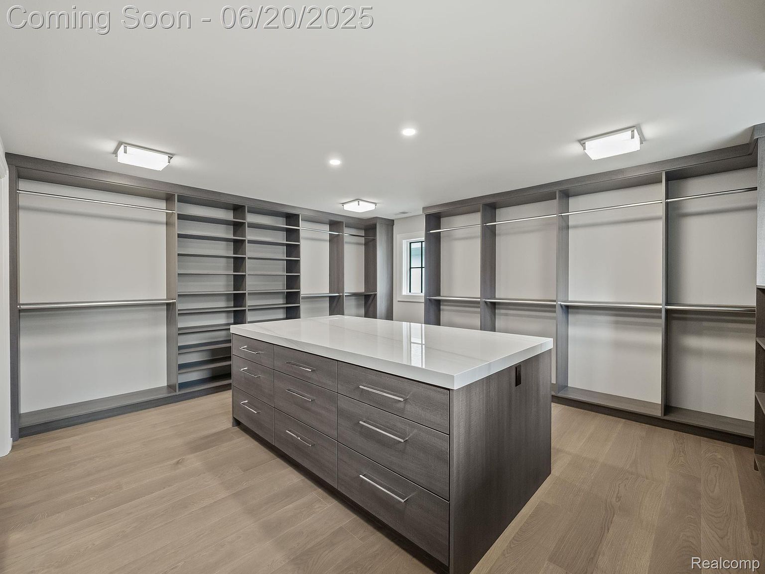 This is a spacious walk-in closet featuring custom shelving and hanging rods, providing ample storage. A central island with drawers offers additional organization space, and the light wood flooring adds warmth to the room. The overall impression is one of luxury and organization.