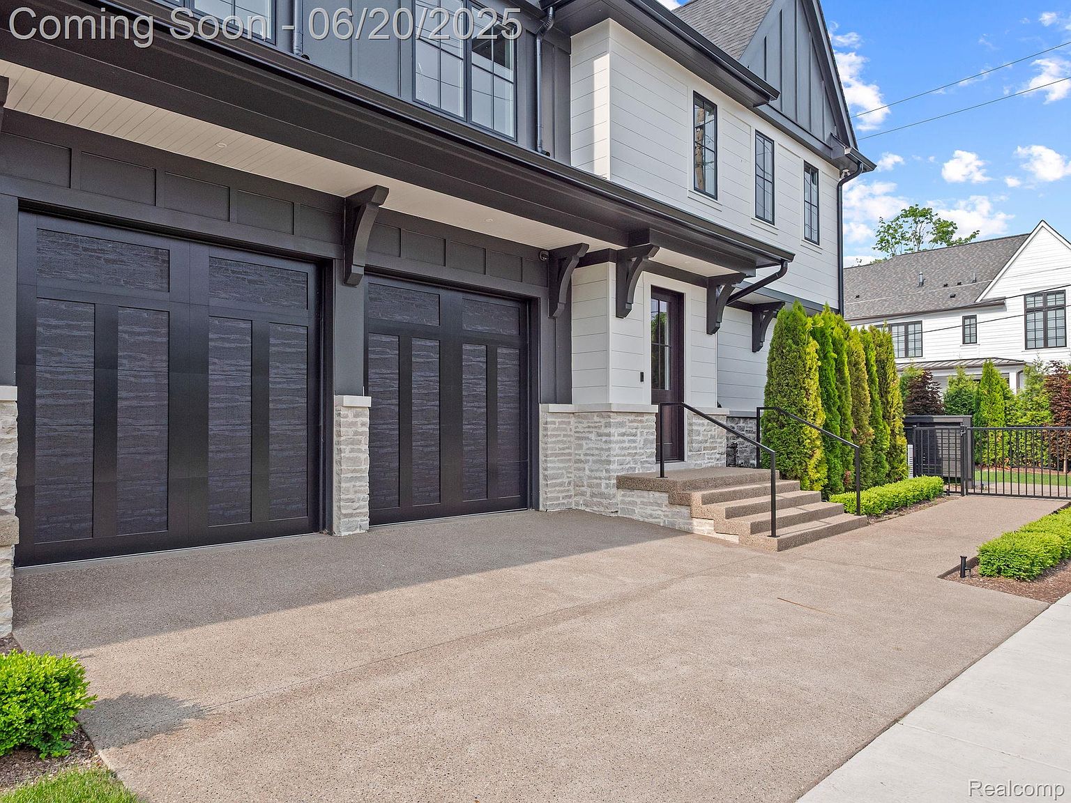 This is a front exterior view of a modern two-story home with a two-car garage. The house features a white facade with black trim, including black garage doors and window frames. A well-manicured lawn and landscaping add to the property's curb appeal, creating a welcoming and sophisticated impression.