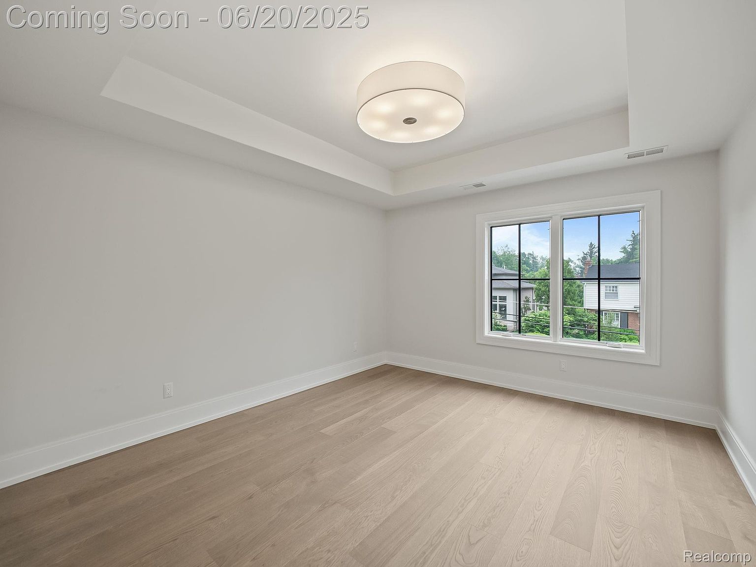 This is a bright and airy bedroom featuring light hardwood floors and white walls, creating a clean and modern aesthetic. A large window provides ample natural light and a view of the outdoors. The room is spacious and uncluttered, offering a blank canvas for potential buyers to envision their own style.