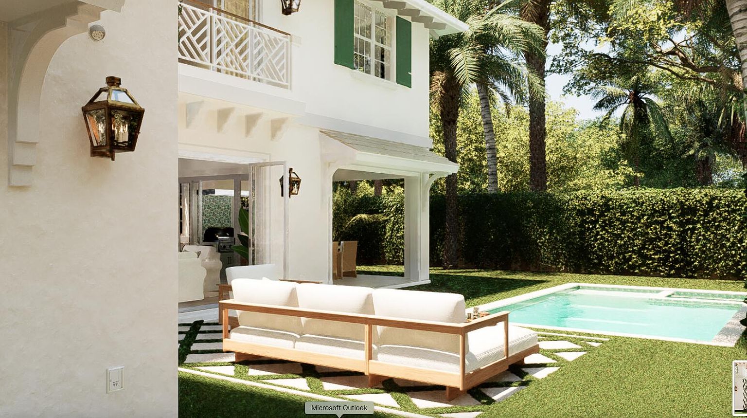 This image showcases the rear exterior of a luxurious home, highlighting a pristine pool and patio area. A comfortable outdoor seating arrangement is positioned on a stone-paved section of the lawn, leading to the pool. The house features white stucco walls, green shutters, and lush landscaping, creating a serene and inviting outdoor living space.