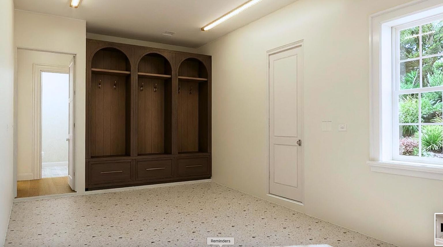 This interior shot showcases a well-organized laundry room featuring custom dark wood built-in lockers with arched tops and drawers. The room has a light-colored terrazzo floor and neutral walls, complemented by a window that provides natural light. A white door adds a clean contrast to the darker cabinetry.