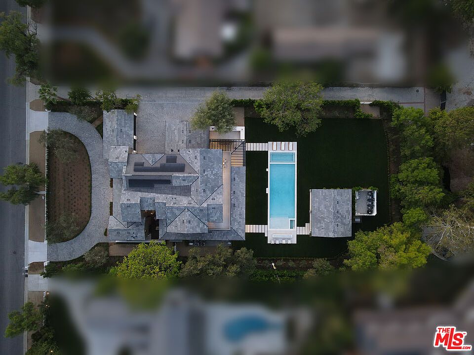 This aerial view showcases a luxurious estate with a sprawling layout. The property features a large house with a complex roofline, a long rectangular swimming pool, a detached garage, and meticulously landscaped grounds. A winding driveway leads to the house, and mature trees provide privacy and shade.
