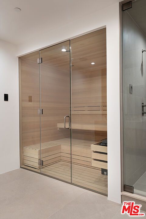 This image showcases a modern sauna with glass doors, featuring wooden benches and paneling. The sauna is well-lit, creating a clean and inviting space for relaxation and wellness. Adjacent to the sauna is a glass-enclosed shower area, enhancing the spa-like atmosphere.