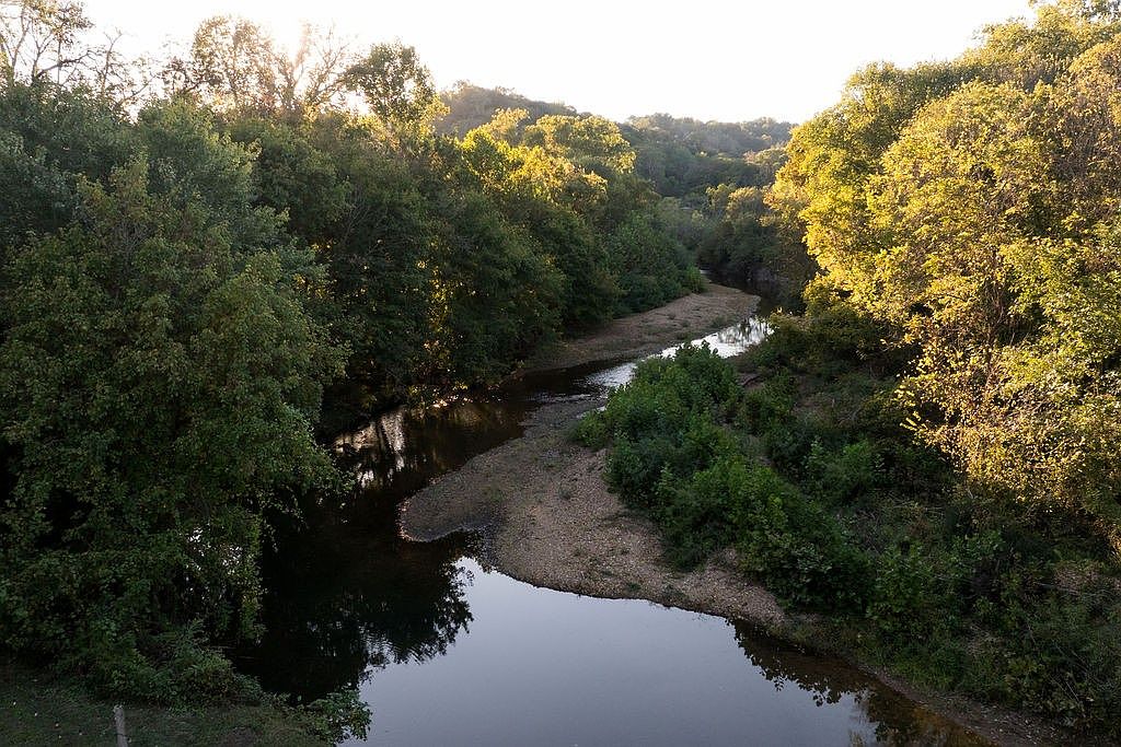 This image showcases a serene river winding through a lush, green landscape. The banks are lined with mature trees and vegetation, creating a peaceful and natural setting. The water reflects the sky and surrounding foliage, enhancing the overall tranquility and highlighting the property's connection to nature.