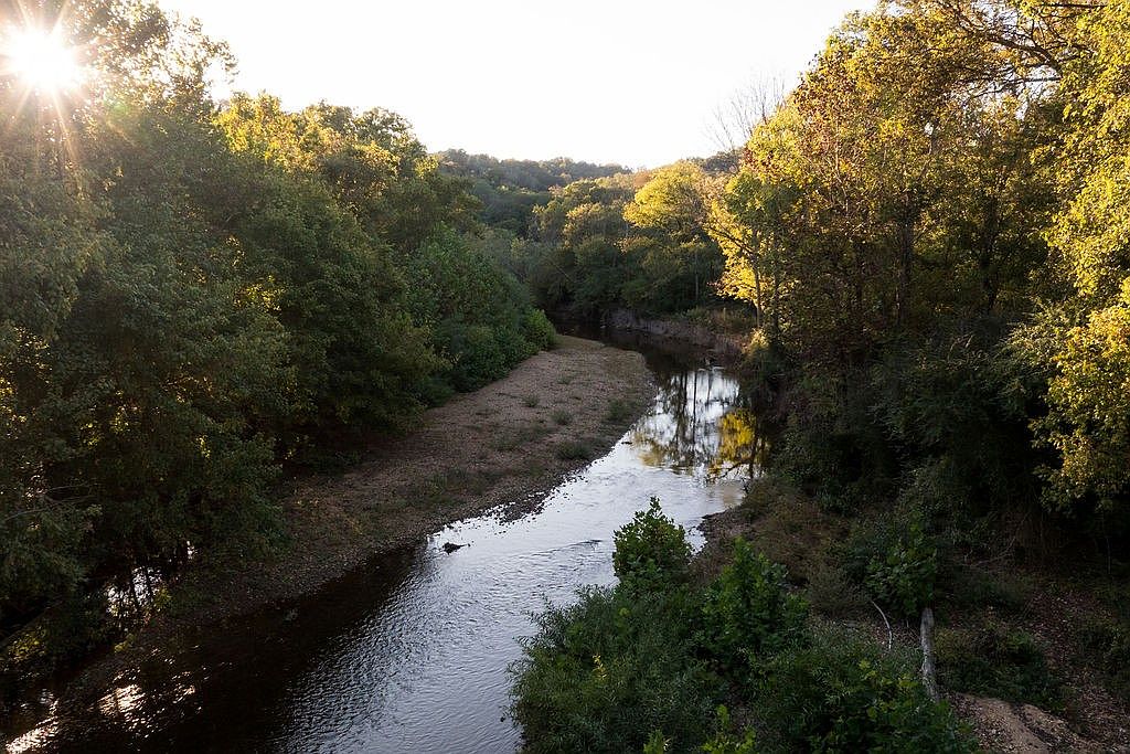 This image showcases a serene river flowing through a lush, green landscape. The sun's rays filter through the trees, creating a dappled light effect on the water and surrounding foliage. The scene evokes a sense of tranquility and natural beauty, highlighting the property's access to a peaceful outdoor environment.