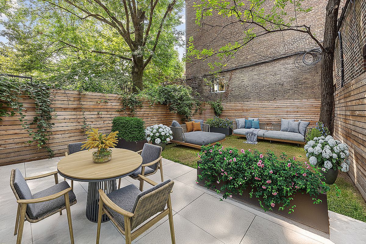 This image showcases a beautifully designed backyard garden, featuring a wooden fence, lush greenery, and stylish outdoor furniture. A round dining table with chairs sits on a paved patio, while a lounge set and sofa offer comfortable seating on the grass. The garden is well-maintained and provides a serene and inviting outdoor living space.