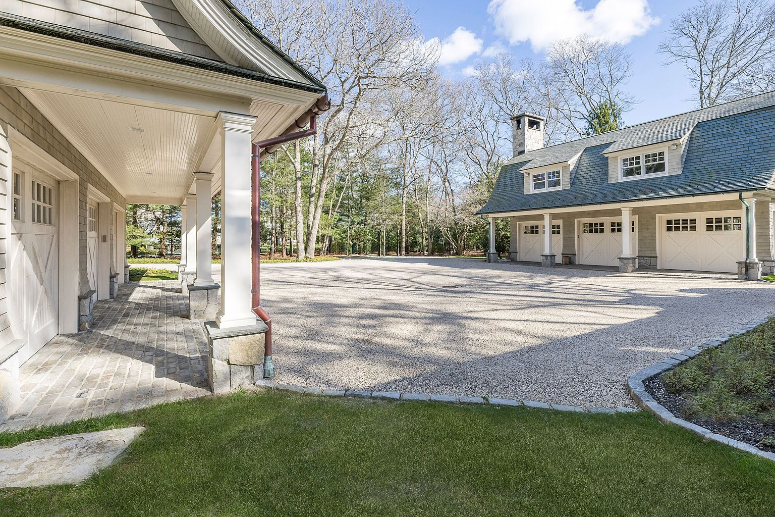 This image showcases a well-maintained garage exterior with multiple bays, suggesting ample parking or storage space. The garages feature a classic design with white doors and trim, complemented by a gravel driveway and manicured lawn. The overall impression is one of a spacious and elegant property.