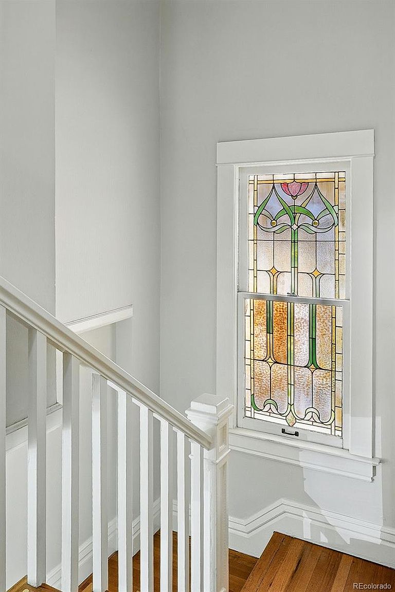 This image showcases a well-lit hallway and staircase area, featuring a white railing and wooden steps. A stained glass window adds a touch of elegance and character to the space, while the white walls create a bright and airy atmosphere. The perspective is from the bottom of the stairs looking up.