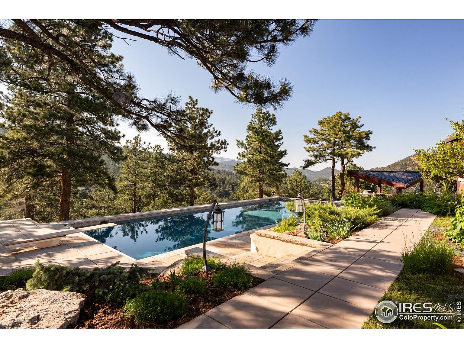 This image showcases a luxurious outdoor pool area with a stunning view of the surrounding landscape. The pool is surrounded by a stone patio and lush greenery, creating a serene and inviting atmosphere. A covered structure is visible in the background, adding to the overall appeal of the property.