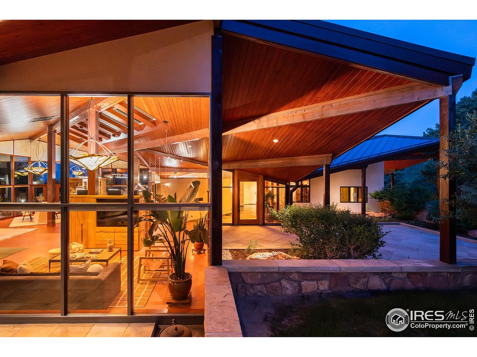 This image showcases a beautifully designed patio area connected to a modern home. The patio features stone flooring, a low stone wall, and lush landscaping, creating an inviting outdoor space. Large windows offer a glimpse into the home's interior, highlighting the seamless integration of indoor and outdoor living.