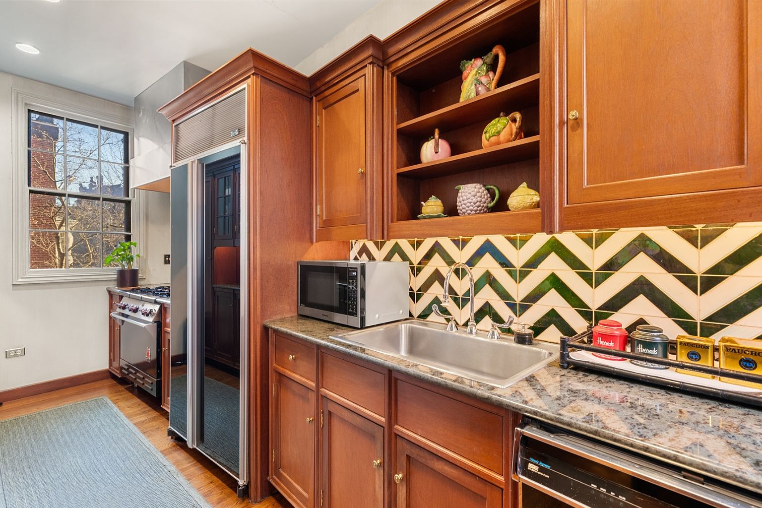 This is a well-appointed kitchen featuring custom wood cabinetry, granite countertops, and stainless steel appliances. The backsplash is a unique chevron pattern, adding a touch of character. The kitchen has a classic and elegant feel, with ample storage and workspace.