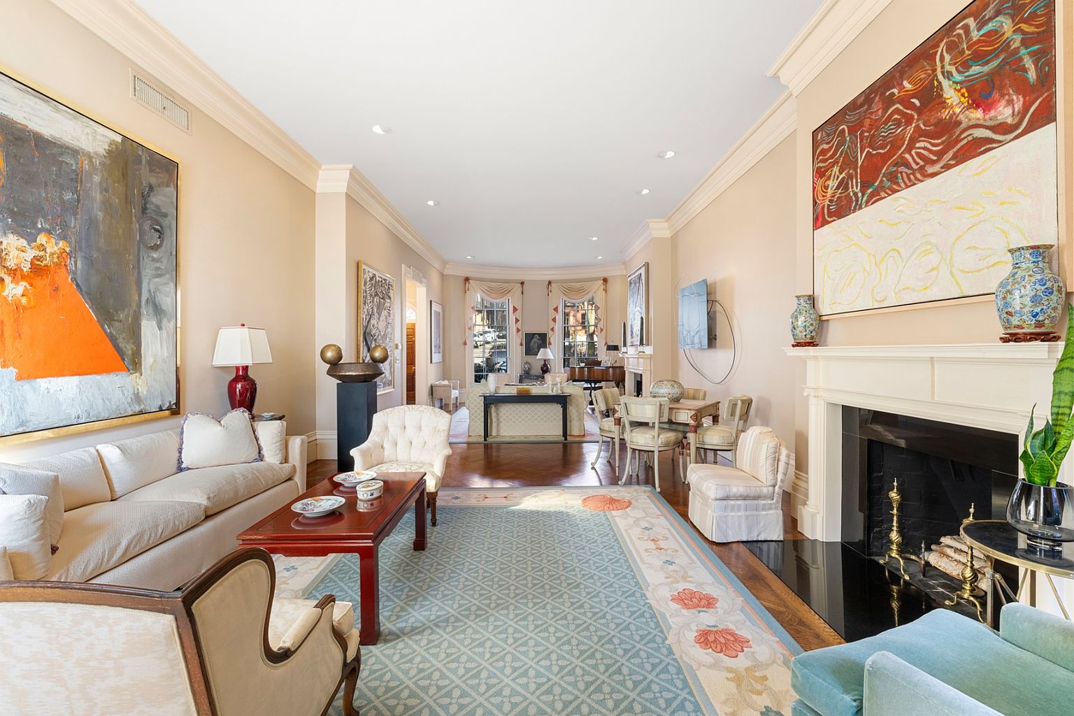 This is a spacious and elegant living room featuring hardwood floors, a large area rug, and neutral-toned walls. The room is furnished with a comfortable sofa, armchairs, a coffee table, and a fireplace, complemented by artwork and decorative vases. The overall impression is one of refined comfort and sophistication, ideal for entertaining or relaxing.