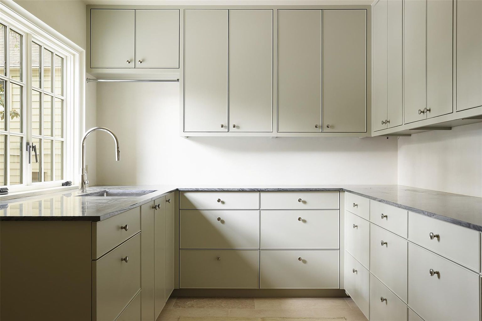 This is a well-organized laundry room featuring light-colored cabinetry with sleek hardware and dark countertops. A stainless steel faucet is visible near a sink, and a window provides natural light. The room appears clean and functional, ideal for a modern home.