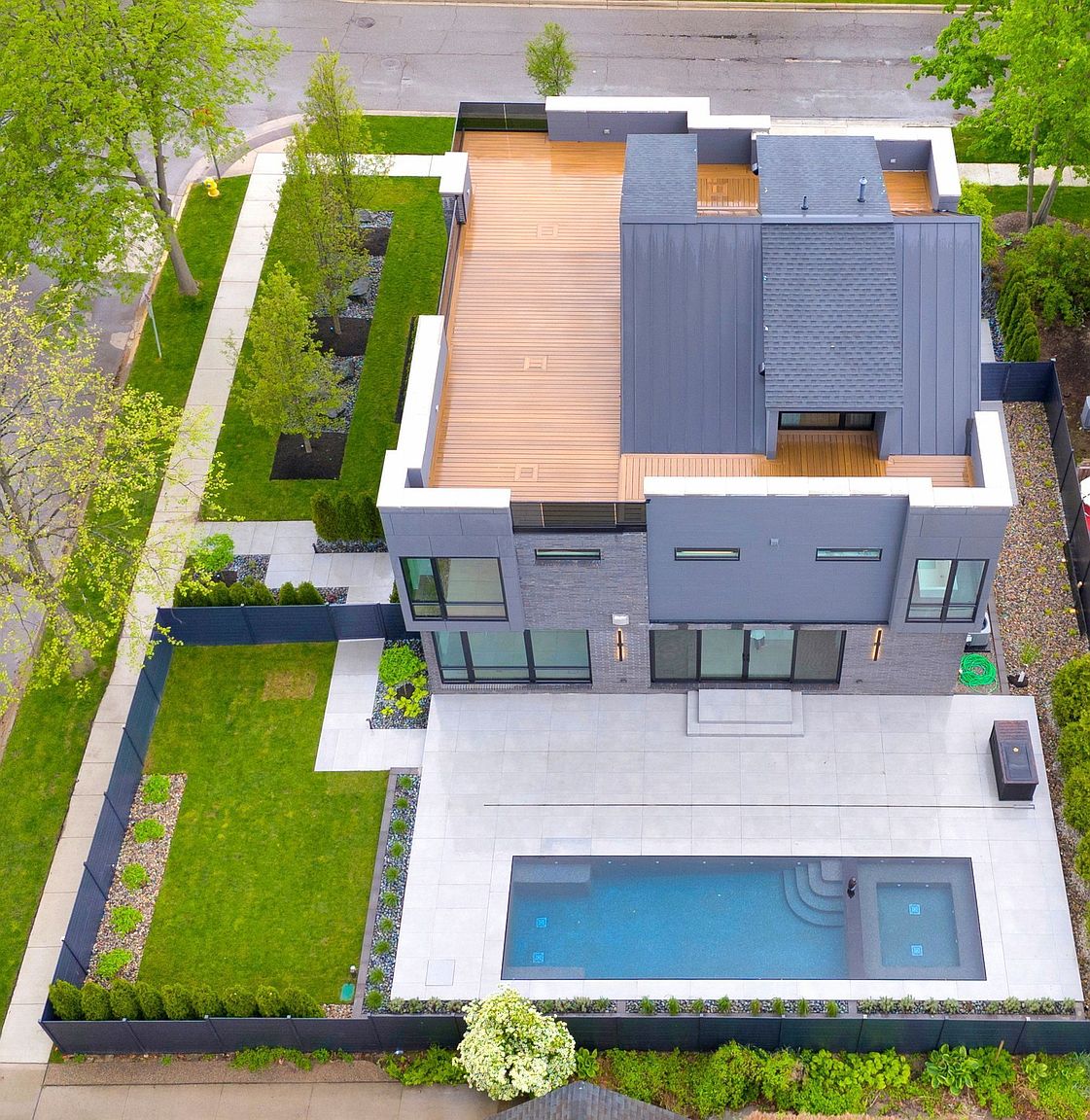 This aerial view showcases a modern home with a striking architectural design. The property features a combination of wood and metal roofing, a backyard pool with a patio, and meticulously landscaped grounds with lush greenery. The clean lines and contemporary aesthetic create a luxurious and inviting atmosphere.