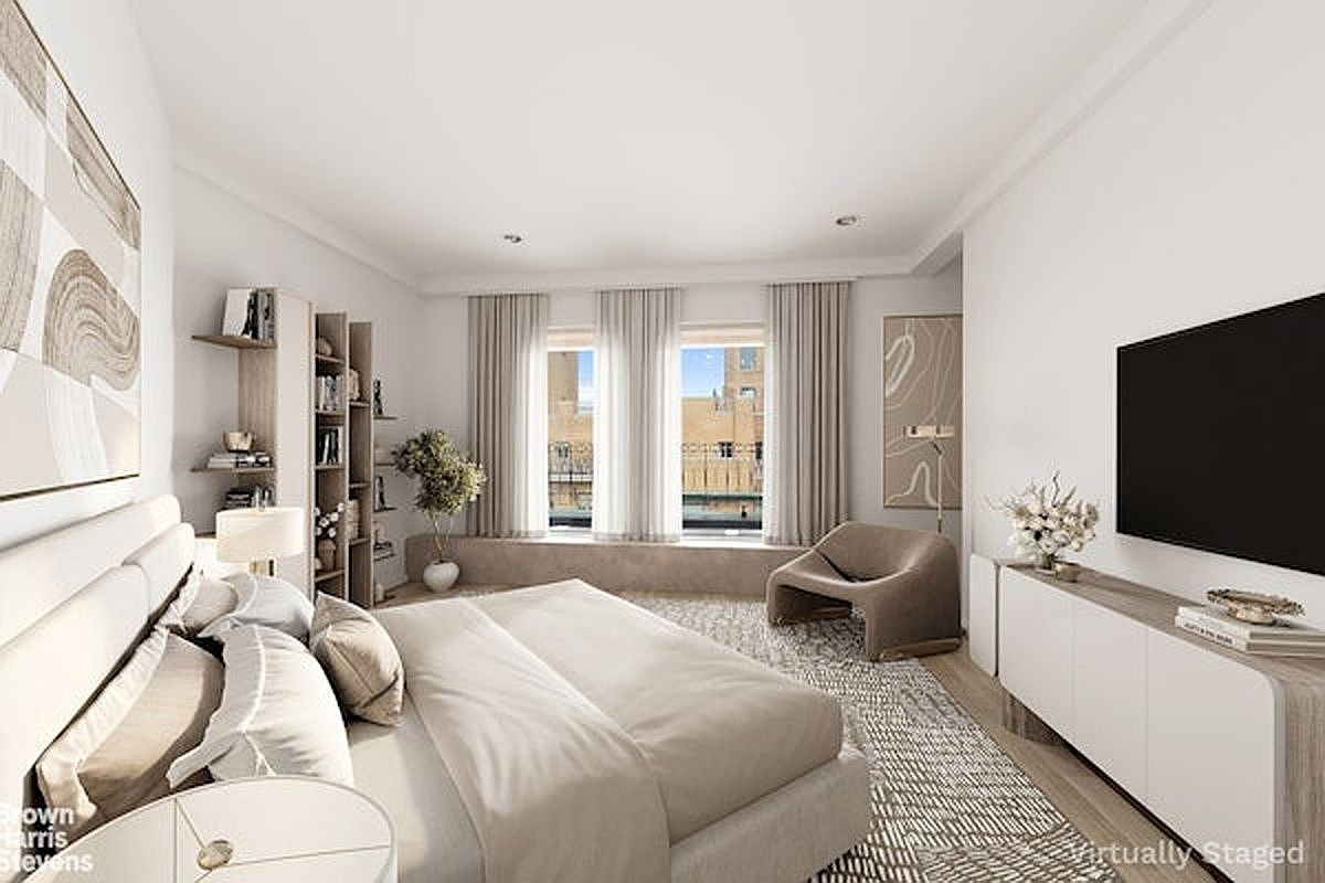 This spacious primary bedroom features a neutral color palette and a contemporary design aesthetic. A large bed with plush bedding serves as the focal point, complemented by a sleek media console, a modern armchair, and built-in shelving units. The room is bathed in natural light from large windows that overlook an urban cityscape, creating an airy and sophisticated atmosphere.