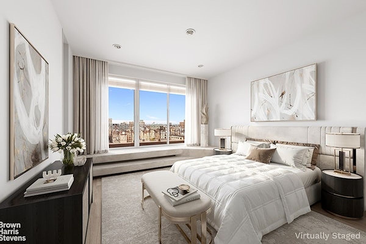This bright and airy primary bedroom features a neutral color palette with a plush bed centered against a tufted headboard. Large windows provide an expansive city view, while a sleek bench sits at the foot of the bed and a dark wood console table adds contrast to the room. The space is elegantly staged with soft textiles and abstract wall art, creating a sophisticated and tranquil atmosphere.