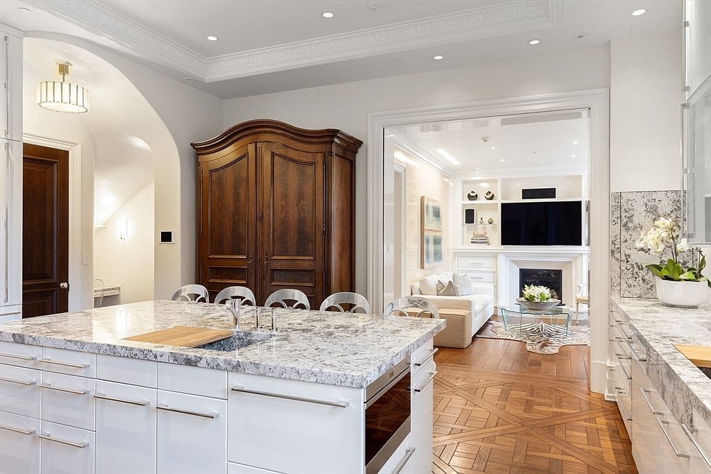 This interior shot showcases a luxurious kitchen with a large island featuring a granite countertop and white cabinetry. The kitchen opens into a living room with a fireplace and built-in shelving, creating a seamless flow. The hardwood flooring adds warmth, and the overall design exudes elegance and sophistication.