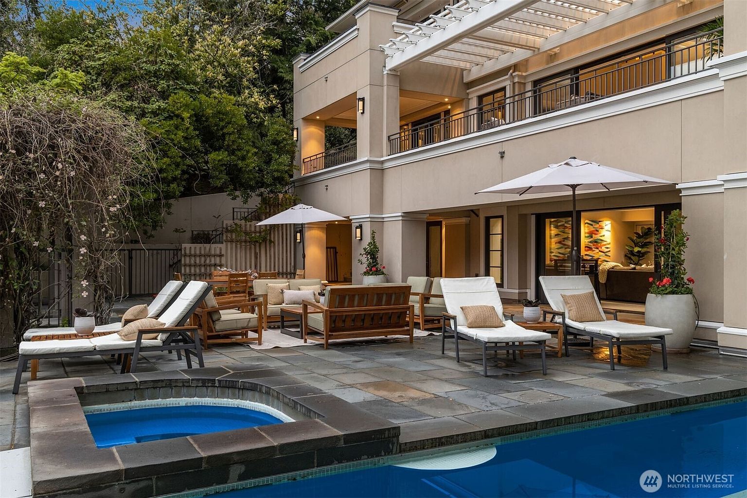 This image showcases a luxurious outdoor living space featuring a pool and spa area. The patio is furnished with comfortable lounge chairs and seating arrangements, perfect for relaxation and entertainment. The architecture of the building includes a covered balcony and large windows, enhancing the indoor-outdoor flow.