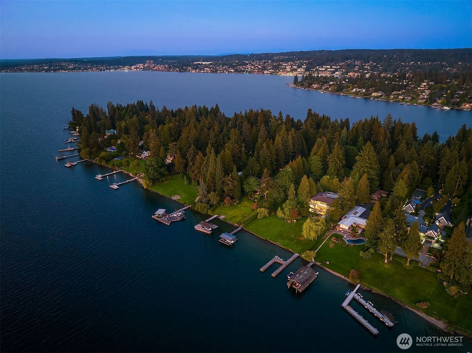 This aerial view showcases a luxurious waterfront property nestled among lush greenery. The estate features multiple docks extending into the calm water, suggesting ample space for boating and water activities. The homes are well-maintained with manicured lawns, offering a sense of privacy and exclusivity.