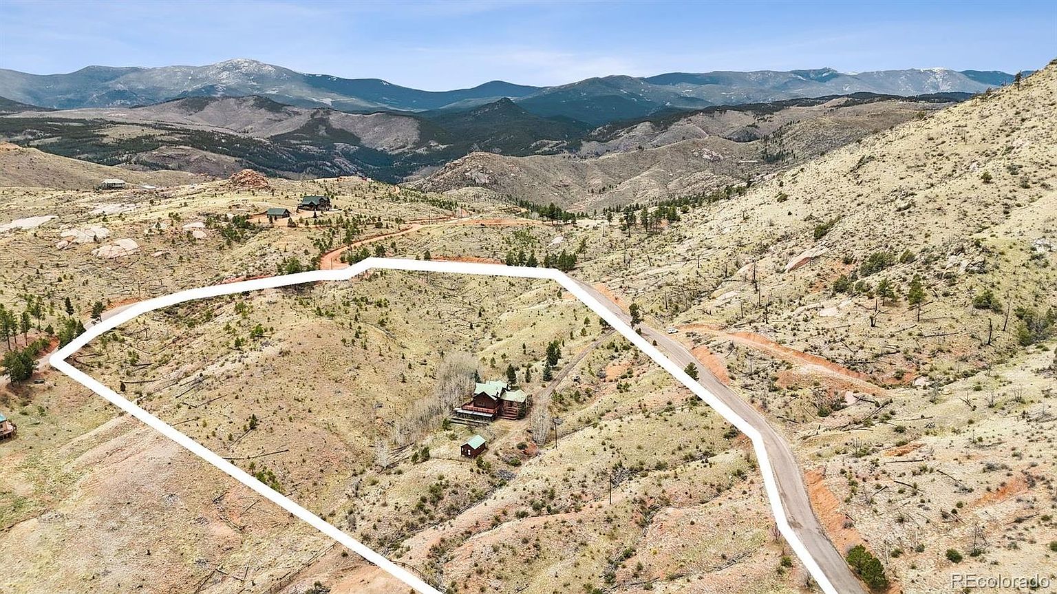 This aerial shot showcases a property nestled in a mountainous landscape. The home, surrounded by trees, is situated within a defined property line, highlighting the expansive land. A winding road provides access, and the overall impression is one of seclusion and natural beauty.