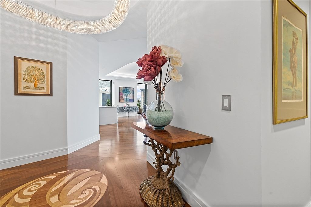 This interior shot showcases a stylish hallway with hardwood floors and decorative inlays. A unique console table with a coral-inspired base holds a vase of flowers, while artwork adorns the walls. The space is well-lit and exudes a sophisticated, welcoming ambiance.