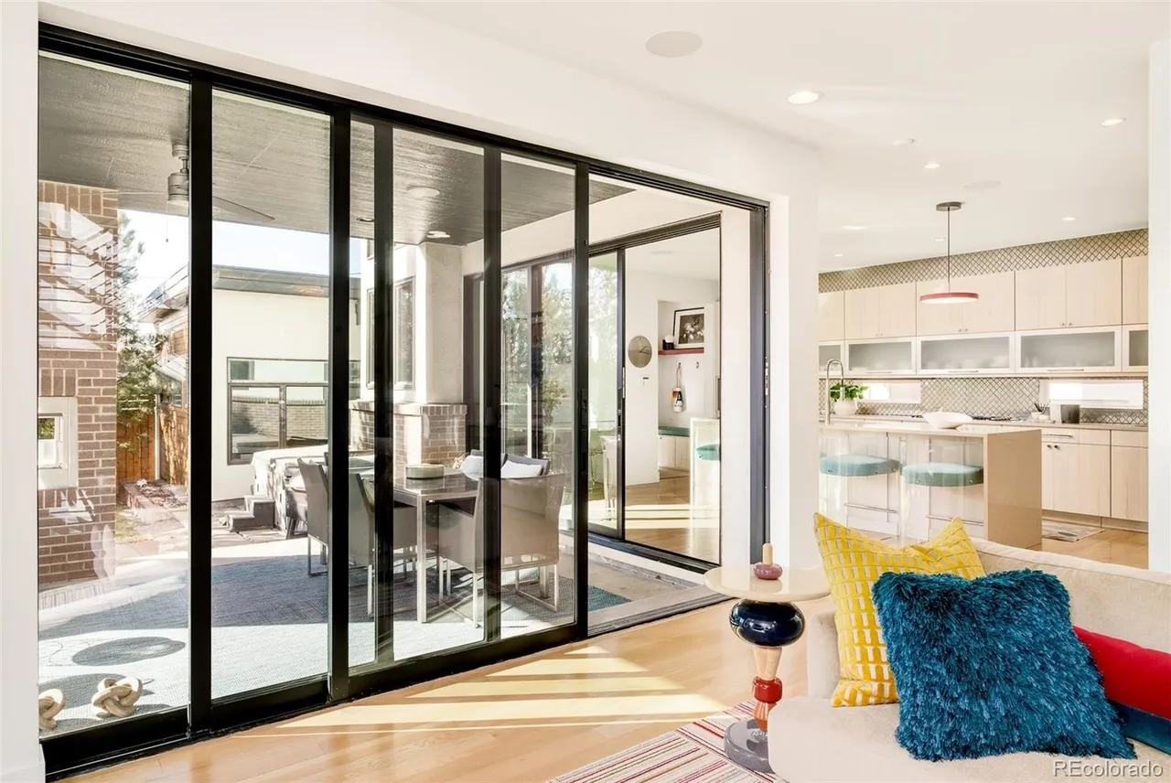 This interior shot showcases a bright and airy living room that seamlessly connects to an outdoor patio through large sliding glass doors. The open-concept design flows into a modern kitchen, creating an inviting and spacious atmosphere. The room is furnished with a comfortable sofa adorned with colorful pillows, adding a touch of warmth and personality to the contemporary space.