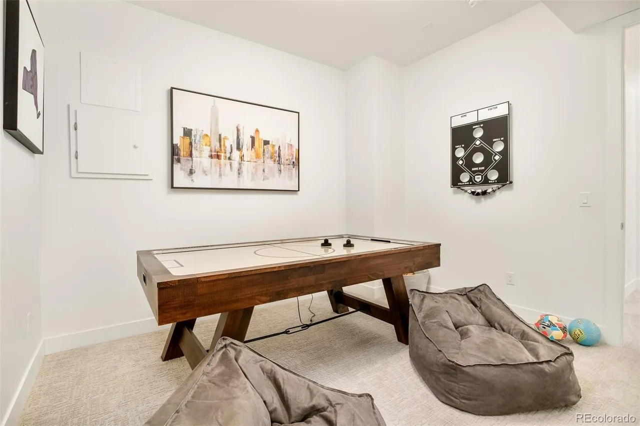 This interior shot showcases a finished basement area, likely a recreation room, featuring an air hockey table as the focal point. The room is decorated with modern artwork and a baseball-themed game on the wall, complemented by comfortable beanbag chairs. The space is well-lit and appears inviting for leisure activities.